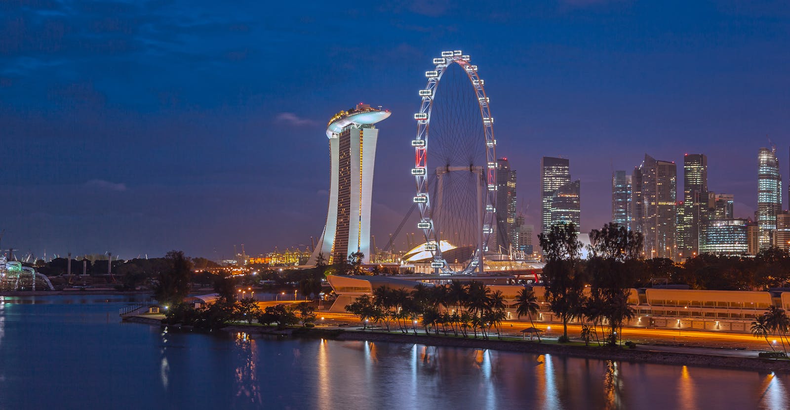 Stunning night view of Singapore with Marina Bay Sands and Ferris Wheel, reflecting city lights on water.